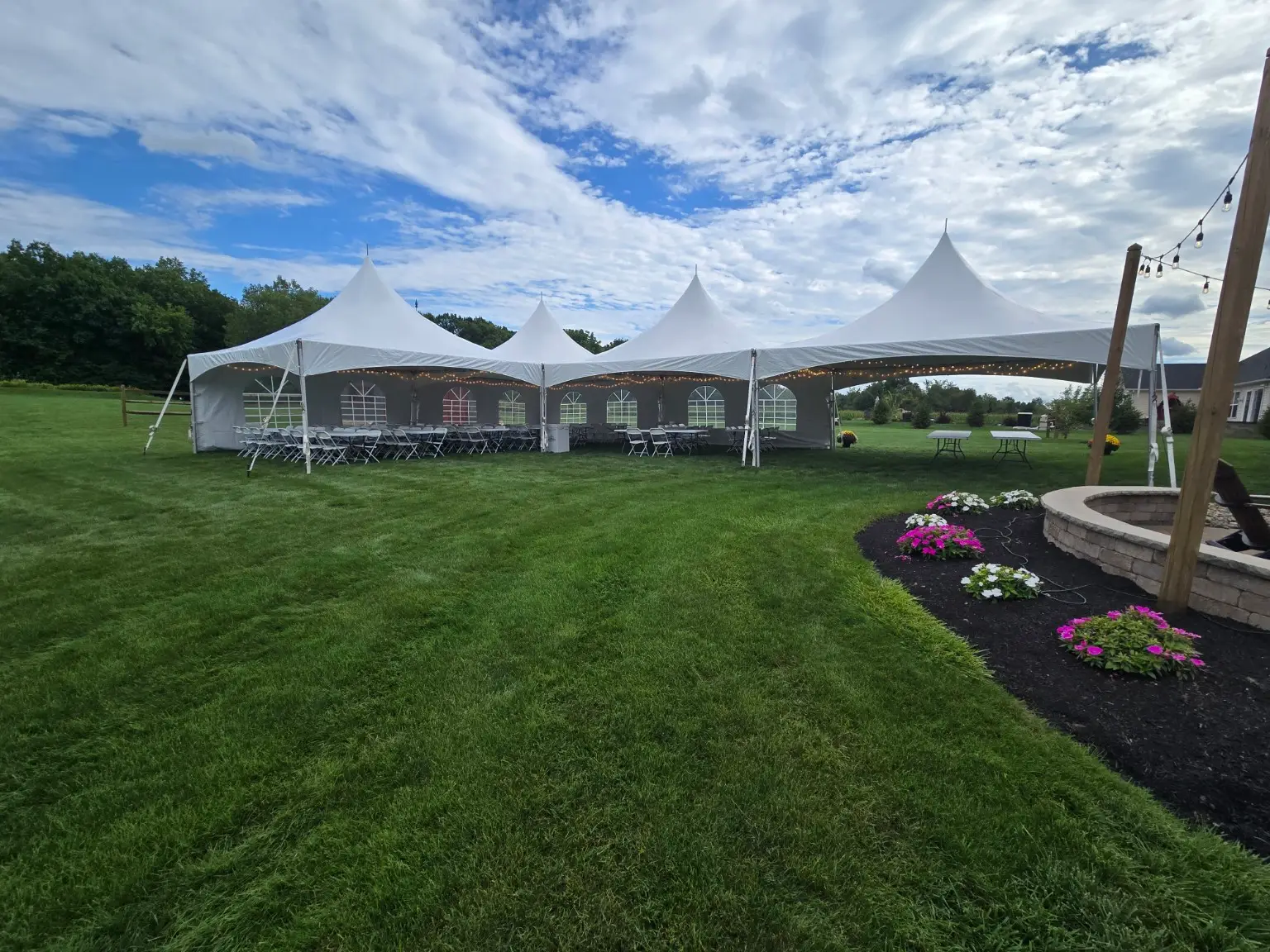 White high-peak tents with tables, folding chairs, sidewalls and string lights on grass
